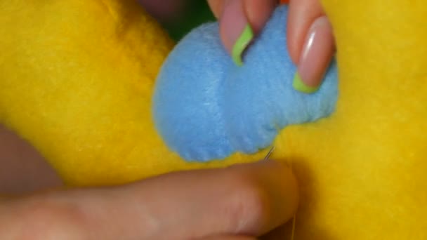 De vrouwelijke handen van een naaister met een manicure naaien op een blauw stuk van een geel speeltje. Naaiatelier, speelgoedfabriek — Stockvideo