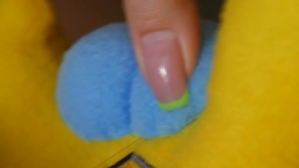 En sömmerskas kvinnliga händer med manikyr syr fast en blå bit av en gul leksak. Syverkstad, leksaksfabrik — Stockvideo
