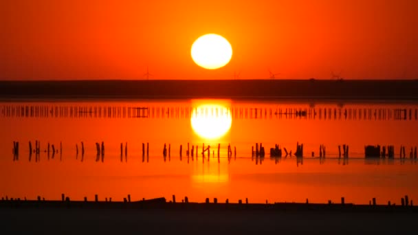 İnanılmaz kırmızı gün batımı. Tuz gölünün üzerinde kocaman yuvarlak bir güneş. Yel değirmenlerinin siluetinin arka planına karşı. — Stok video