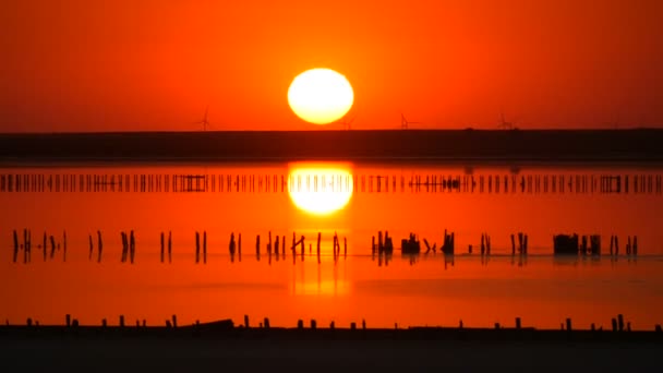 風車のシルエットを背景に塩湖に巨大な丸い太陽が沈む素晴らしい赤い夕日 — ストック動画