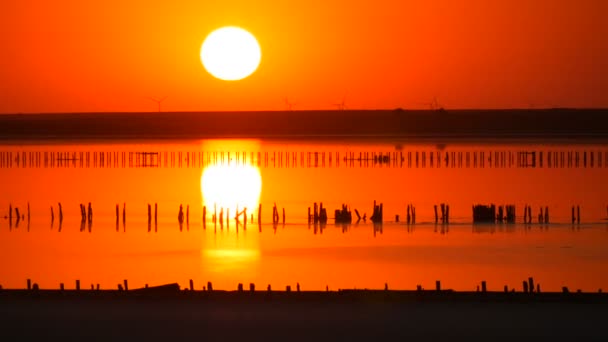 İnanılmaz kırmızı gün batımı. Tuz gölünün üzerinde kocaman yuvarlak bir güneş. Yel değirmenlerinin siluetinin arka planına karşı. — Stok video