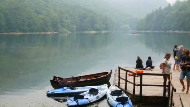 Nationaal Park Biogradska Gora, Montenegro - 24 augustus 2020: ligplaats met mensen en houten boten op een ongelooflijk mooi meer met een mistige ochtendwaas. Bergvijver Biorgad Lake — Stockvideo
