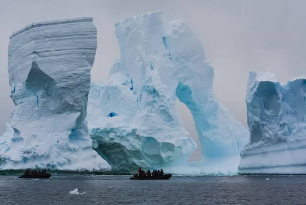 People on boats sailing along icebergs. People on boats sailing along icebergs.
