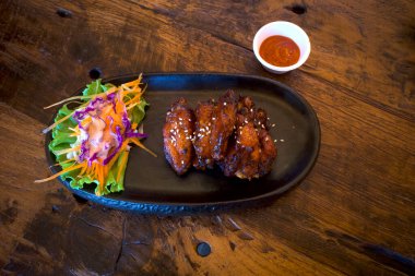 Koyu bir tabakta iştah açıcı tavuk kanatları, susam tohumları serpilmiş ve sebze ve biber sosuyla süslenmiş..