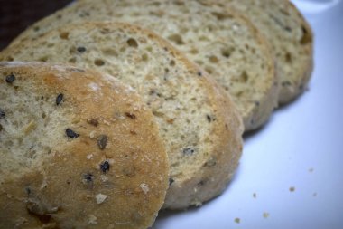 Tam buğday ekmeği, tohumlu, beyaz tabakta kesilmiş, sağlıklı ekmek seçimi..