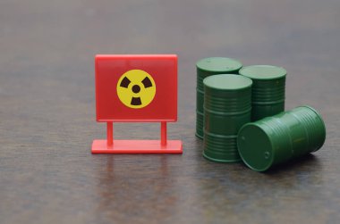 Yeşil variller, nükleer atık ve tehlikeli maddelerin risklerini güçlü bir şekilde sembolize eden radyasyon sembollü kırmızı bir tabelanın arkasında otururlar..