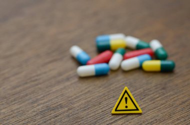 Üzerinde ünlem işareti olan uyarı işareti bulanık renkli hapların önünde duruyor, reçeteli ilaçların doğal tehlikelerini simgeliyor..