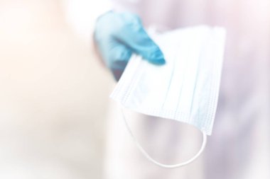 Plastik eldiven takan bir doktor ya da bilim adamının elleri cerrahi yüz maskesini kameranın önüne kadar uzatıyor..