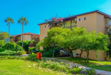 Tatil konsepti. Yaz tatilleri arka plan. Ev, sokak, ağaçlar, çimenler, çiçekler ve mavi gökyüzünün canlı fotoğrafı