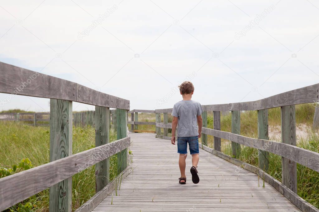 Child is alone on the road. Boy is lost and goes forward. Boy wants to be alone. Back view of a child demonstrating resentment and walking away