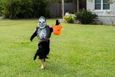 Cute little boy in halloween skeleton costume. Little boy in skeleton costume with pumpkin candy bucket trick or treating outside. clipart