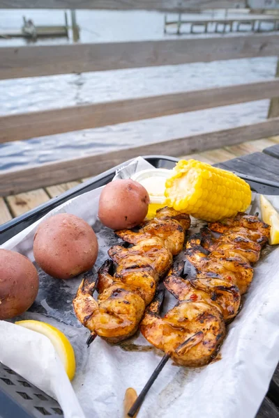 Fast food seafood. Barbecue shrimp, steamed corn and jacket potatoes. Traditional seafood, vegetables and lemon slices in disposable dishes in restaurant on the beach.