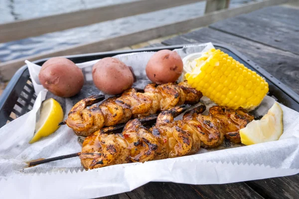 Junk food seafood. Barbecue shrimp, steamed corn and jacket potatoes. Traditional seafood, vegetables and lemon slices in disposable dishes in restaurant on the beach.