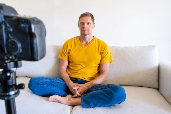 Happy handsome young male speaker sitting in front of camera recording webinars training videos at home. Smiling experienced guy make a video for his blog.