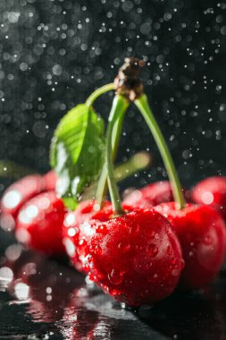 Koyu arkaplanda su damlaları olan taze kırmızı kirazlar, yakın plan görünüm..