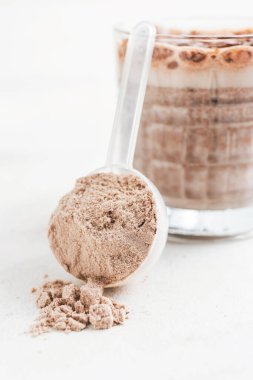 Beyaz protein tozu ölçme kaşığında bir bardak çikolatalı protein içeceği, beyaz masada milkshake smoothie..
