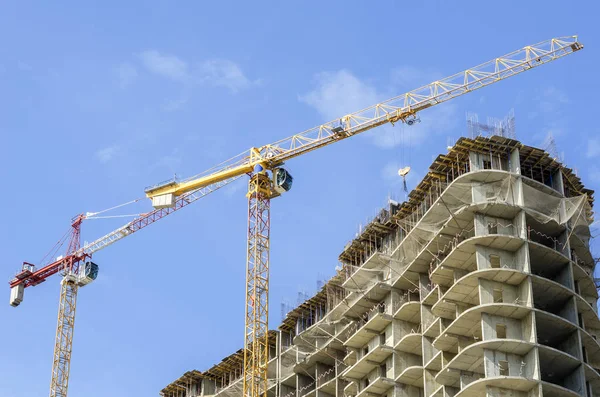 Two construction cranes on a background of blue sky and a concre — Stock Photo, Image