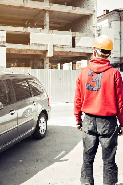 Construction worker with protection helmet in black and red clothes inspecting the building site