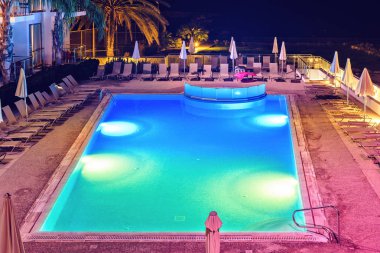 Otel havuzuna parlak renkli ışıkları ile gece görünümü üstten. Şezlong ve arka plan avucunda. Protaras, Kıbrıs