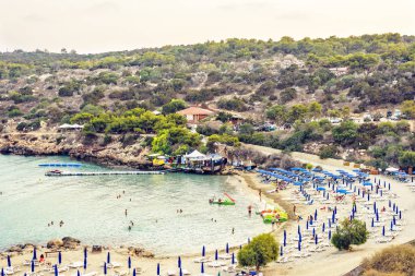 Protaras, Kıbrıs - 16 Eylül 2018: Gün ışığı günbatımı manzaralı Konnos Plajı'na kum üzerinde rahatlatıcı ve suda yüzen insanlar. Su ulaştırma araçları yola yakın kira. Arka planda dağlar