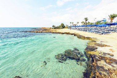 Nissi Beach yaz görünümüne renkli parlak mavi su ve gökyüzü bulutlu. Yüzme ve kum üzerinde rahatlatıcı turistler. Negatif kopya alanı, metin için yer. Ayia Napa, Kıbrıs