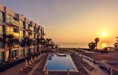 Protaras, Kıbrıs - 20 Eylül 2017: Coral Bay resort yukarıda sıcak gündoğumu görünümüne. Otel Havuzu, palmiye ağaçları, tekne ve deniz arka plan üzerinde. Negatif kopya alanı, metin için yer