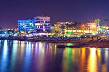Gece cityscape ile beachline, ışıklar binalar üzerinde parlayan ve su üzerinde yansıtan. Negatif kopya alanı, metin için yer. Protaras, Kıbrıs