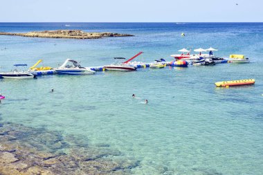 Protaras, Kıbrıs - 23 Eylül 2017: Gün ışığı görünümüne Park edilmiş tekneler ve küçük pier yakınındaki şişme oyuncaklar. Suda yüzen insanlar. Negatif kopya alanı, metin için yer