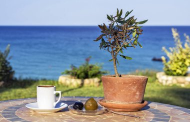 Kahve gün ışığı görünümüne tablo yerel tatlılar, zeytin ağacı ve kaşık. Deniz manzaralı ve gökyüzü arka plan üzerinde. Protaras, Kıbrıs Adası