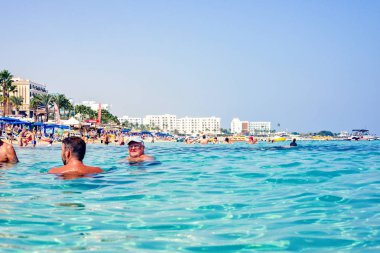Ayia Napa, Kıbrıs - 18 Eylül 2017: Gün ışığı manzara denizin berrak suda yüzen insanlar için. Arka plan üzerinde otel ve palmiye ağaçları. Negatif kopya alanı, metin için yer. Nissi Beach