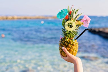 Ananas meyve ve mini bir şemsiye ile harika egzotik bir tarzda dekore edilmiştir. Meyve tutun iki kadın eli tarafından ediliyor. Deniz arka plan üzerinde. Nissi Beach, Ayia Napa, Kıbrıs.