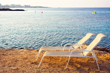 Güneşlenme sandalyeli günbatımı görünümüne. Şehir ve deniz içinde belgili tanımlık geçmiş. Negatif kopya alanı, metin için yer. Ayia Napa, Kıbrıs.
