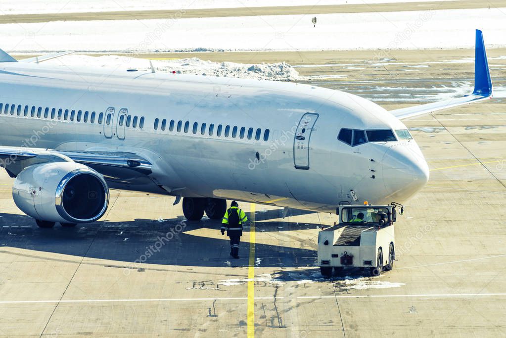 Unbranded plane pushing back from gate with workers controlling front tire direction