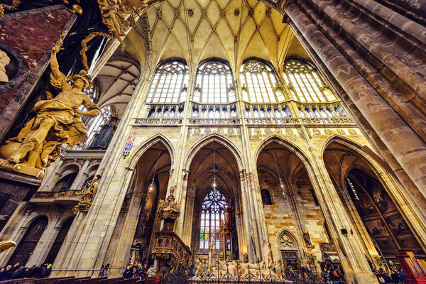 PRAGUE, CZECH REPUBLIC - MARCH 23, 2018: Gothic architecture interior of St. Vitus Cathedral with glowing windows and drawings on walls. Tourists exploring the church