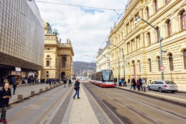 Prague, Çek Cumhuriyeti - 24 Mart 2018: insanlar kaldırım ve arabalar yolda sürme. Kırmızı tramvay yolcu için bekliyor. Eski mimari yapılar yansıtan parlak güneş