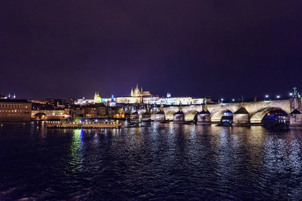 Prag Kalesi ve Charles Köprüsü ile parlayan ve su üzerinde yansıtan ışık gece. Negatif kopya alanı, metin için yer. Çek Cumhuriyeti