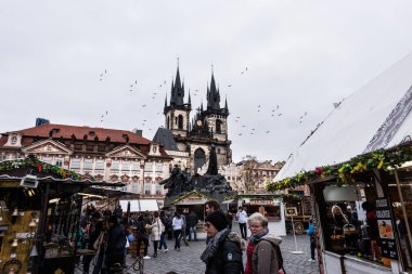 Prague, Çek Cumhuriyeti - 24 Mart 2018: kilise Our Lady Tyn tarihi kent Meydanı'nda önce. Kuledeki uçan kuşlar. Turistler yerel tezgahları keşfetmek. Dramatik renkler. Bulutlu ve yağmurlu bir gün