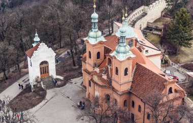 Petrin Tepesi'nde dramatik renklerle St Lawrence Kilisesi. İnsanlar önünde yürürken, insanlar. Karanlık ağaçlar kurumuş. Prague, Çek Cumhuriyeti