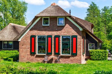 Güneşli bir günde rustik thatched çatı ile geleneksel ev. Ağaçlar, çiçekler ve parlak mavi gökyüzü bulutlu arka plan üzerinde. Giethoorn, Hollanda