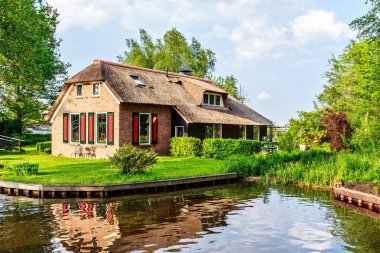 Güneşli bir günde alt yerel nehirden. Ağaçlar, geleneksel evler ve parlak mavi gökyüzü bulutlu arka plan üzerinde. Negatif kopya alanı, metin için yer. Giethoorn, Hollanda