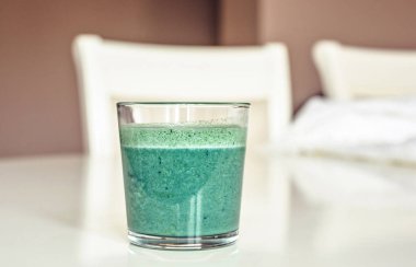Spirulina sallamak bir bardak beyaz masada. Arka plan üzerinde sandalye ile yakın çekim vurdu. Negatif kopya alanı, metin için yer. Kişinev, Moldova