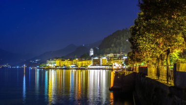 Gece Bellagio şehir. Parlayan ve su üzerinde yansıtan ışık. Arka planda dağlar. İtalya güzellikleri