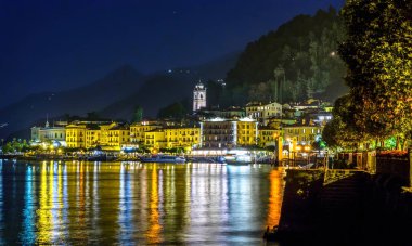 Gece Bellagio şehir. Parlayan ve su üzerinde yansıtan ışık. Arka planda dağlar. İtalya güzellikleri