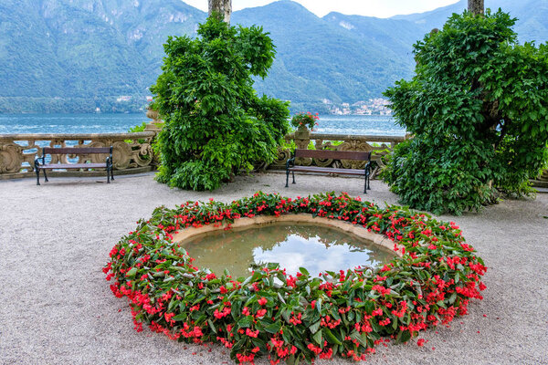 Small pond ornamented with red flowers. Villa del Balbianello green garden