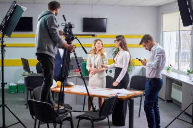 Film yönetmeni, ofis sahnesindeki aktörlerle film planını tartışıyor. Işıklar aktörleri gösteriyor.