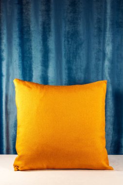 Masanın üzerinde canlı turuncu yastık. Mavi arka plan. Işık castig yumuşak gölgeler sıcak sesi ile. İç tasarım fikir. Dikey vurdu