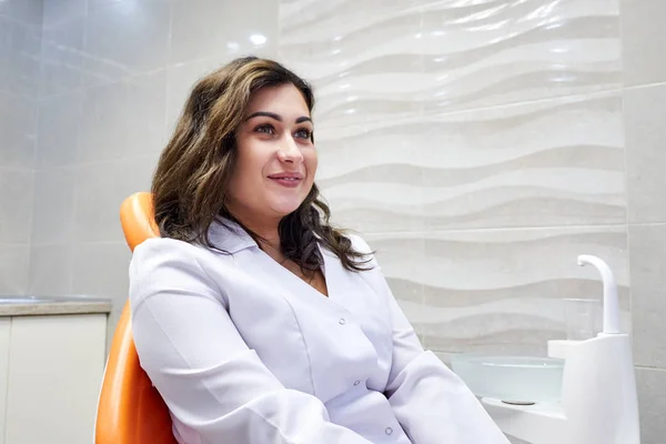 Young female dentist sitting on the chair in dental cabinet