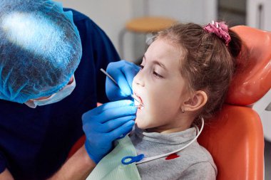 Küçük kızın dişleri inceleyerek erkek diş hekimi