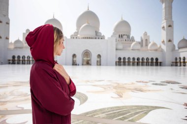 Woman at Abu Dhabi Mosque. Wearing a red Hijab looking at the Sheikh Zayed Grand Mosque in UAE. Sunny day, beautiful architecture views clipart