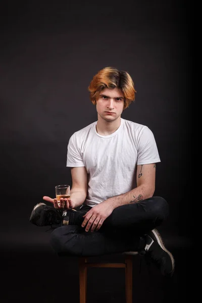 Young caucasian adult with blonde hair holding whiskey in hand